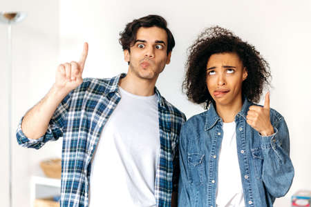 Young funny cheerful couple in love, african american girl and mixed race guy, fool around, make faces, look funny and joyful, having fun togetherの写真素材