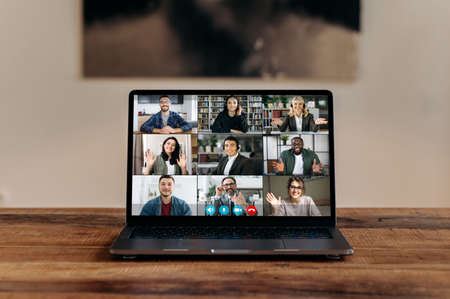 Front view at laptop screen standing on wood desk, with a group of multiracial different people...