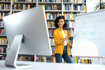 Joyful african american female coach, standing near whiteboard, in casual clothes, conducts an...