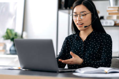 Confident pretty smart asian girl with glasses and headphones, freelancer, call center operator,...