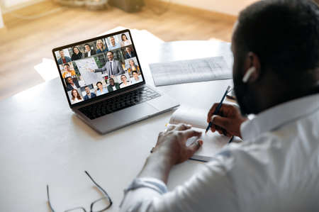 Online business seminar. View over the shoulder of an african american guy taking notes in a...