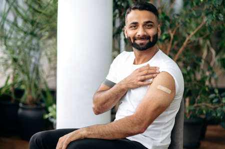 Treatment and prevention, vaccination concept. Vaccination during virus  pandemic and influenza. Satisfied Indian man with a plaster on shoulder after vaccination. Healthcare conceptの写真素材
