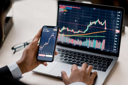 Close-up of a laptop and cellphone screen with diagrams. Crypto trader investor broker using...