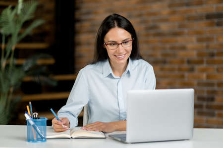 Pretty, smart successful caucasian young brunette woman sit at the work desk, studying or working in...