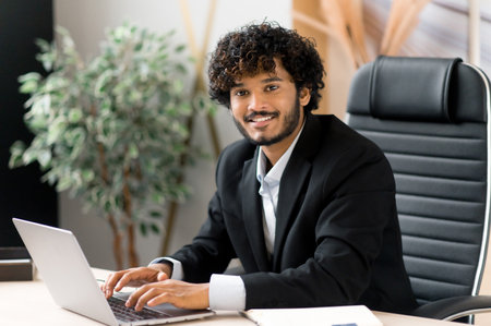 Portrait of happy successful charismatic curly haired young adult Indian businessman, ceo or top...