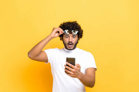 Amazed shocked unshaven Indian or Arabian guy holding smartphone in his hand, looking at the camera...