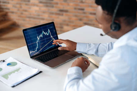 Smart focused african american broker investor, uses laptop to analyze financial cryptocurrency market, invest in e-currency, buy or sell crypto coins, analyze financial data, develop strategyの写真素材