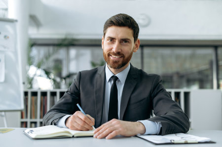 Confident intelligent caucasian businessman, sit in modern office, listening lecture, webinar via video conference, taking notes in a notebook, communicates with business partners, conducts briefingの写真素材