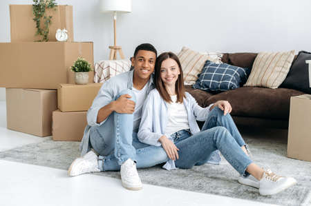 Happy multiracial family couple in love, hispanic guy and caucasian girl, sit on the floor in the...