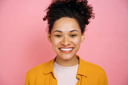 Close-up portrait of young mixed race woman in casual orange t-shirt, african american girl with...