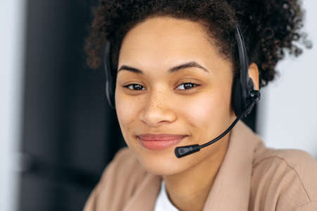 Close-up photo of pretty, confident curly-haired young african american woman with headset, call...