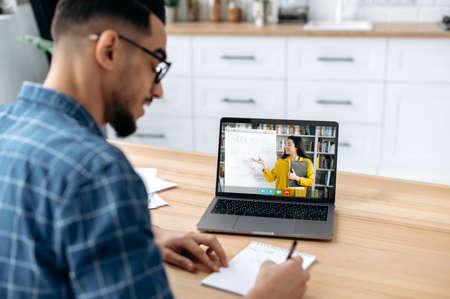Distance online lesson. View over the shoulder of a guy, a student, on a laptop screen with a female...