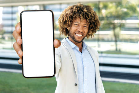 Positive attractive african american or brazilian curly haired man, stands outdoors, shows smart...