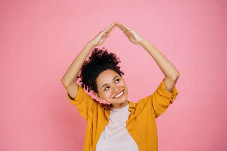 Cheerful pretty, african american curly haired girl in casual clothes, is feeling safe under house...