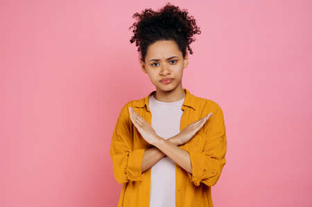 Strict curly haired african american girl in casual clothes, saying no, crossed hands in stop...