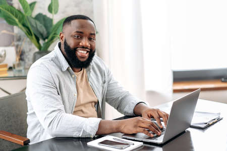 Attractive positive african american stylish man, entrepreneur or freelancer, IT specialist, working...