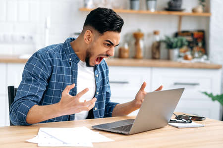 Angry annoyed young man, Arabian or Indian company worker, freelancer, stylishly dressed, working...
