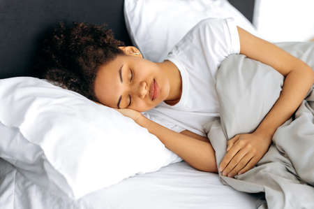 Morning in bed, sweet dreams. Calm African American lovely curly girl, sleeps sweetly in bed, sees...