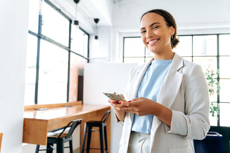 Photo of a positive hispanic or brazilian woman, business entrepreneur, standing in modern office,...
