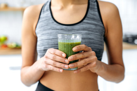 Close-up photo of a green fresh smoothie in a glass cup in female hands. Sporty woman prepared herself a healthy vitaminized smoothie. Healthy eating, veganism, raw food, diet, detoxの写真素材