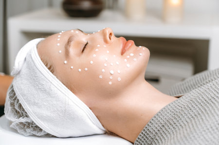 Care procedures in the salon. Side view to female face with moisturizing cream on her face of a young beautiful woman. Anti-aging cream on a females face to prevent premature wrinklesの写真素材