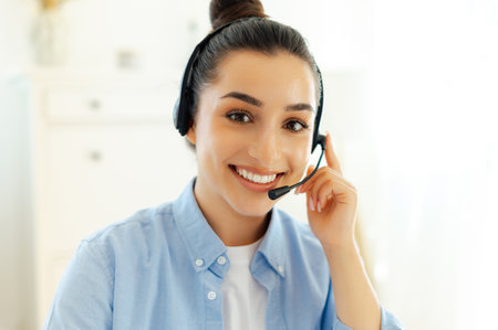 Close-up photo of a joyful gorgeous successful brunette caucasian woman with headset, working as call center operator, customer support service, hotline assistant, smiles at camera friendlyの写真素材