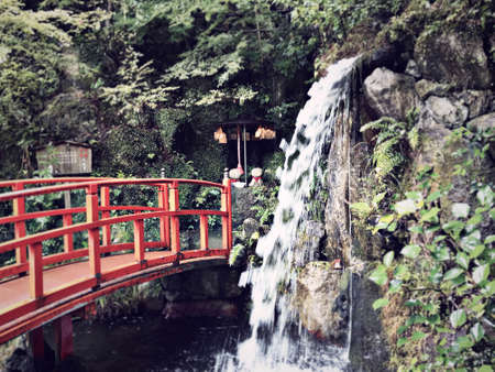 Waterfall and red bridge at a Japanese shrineの写真素材