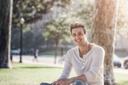 Handsome casual happy man sitting in park.