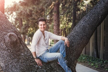 Handsome casual happy man sitting on tree.の写真素材