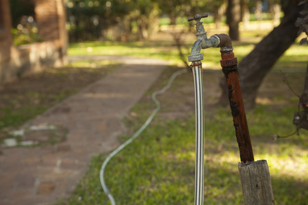 Old rusty water tap with hose in gardenの写真素材