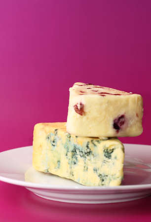 Two pieces of fresh cheese blue stilton and wensleydale and cranberry arranged on white porcelain plate isolated on pink backgroundの写真素材
