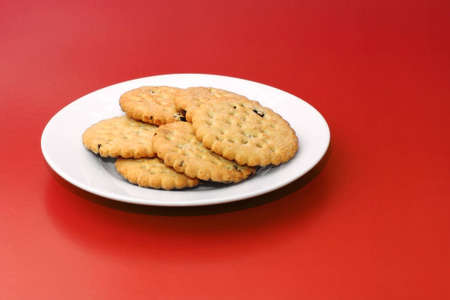 Freshly baked homemade fruit shortcake biscuits arranged on white porcelain plate isolated on red backgroundの写真素材