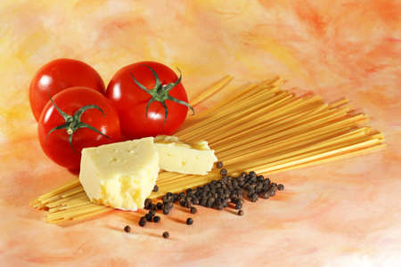 Ingredients used in Italian cuisine including red tomatoes yellow cheese fresh black pepper corns and linguine pasta arranged on abstract orange backgroundの写真素材