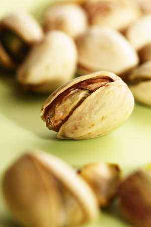 Close-up of pistachio nut in open shell on green background with more pistachios blurred in foregroundの写真素材