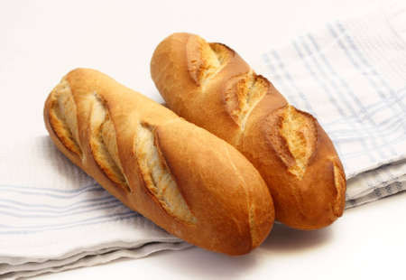 Two long narrow french loafs laid on tea towel on white background