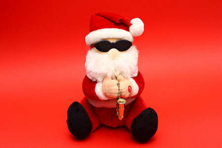 Soft toy Santa Claus wearing shades and playing saxophone on red backgroundの写真素材