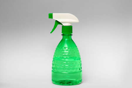 Green spray bottle made of clear plastic isolated on grey background