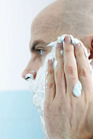 Young man applying shaving foam to face photographed in profileの写真素材