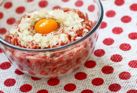Raw pork mincemeat with egg and chopped onion in a clear glass  bowl