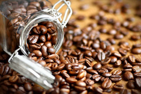 Close up of scattered roasted coffee beans from a clear glass jar
