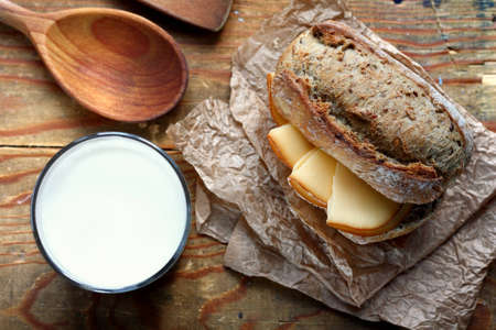 Top view on cut in halves whole grain bread roll with smoked cheese and a glass of milkの写真素材