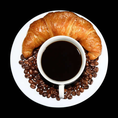 Top view of cup of hot coffee with beans and a crunchy croissant on the side on black backgroundの写真素材