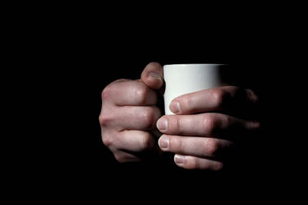 Close up of male hands holding mug with coffee or tea on black backgroundの写真素材
