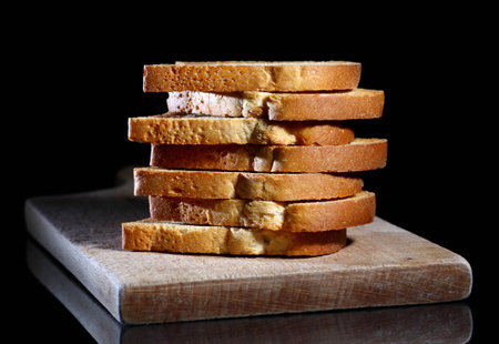 Close up of toasted white bread in slices on cutting board over black backgroundの写真素材
