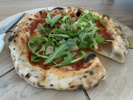 A delicious pizza is presented on a wooden board and table, viewed from the side, with a black background. The ingredients are thoughtfully arranged around it.の写真素材