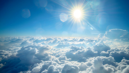 A view from above a sea of clouds with the sun shining brightly in the blue sky.