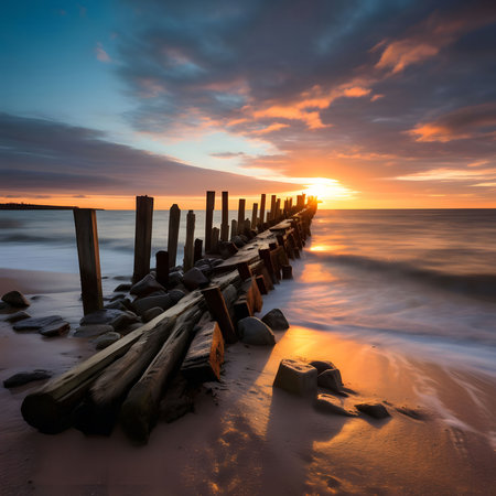A wooden jetty extends into the ocean at sunrise, the golden light reflecting off the water and casting long shadows.の写真素材