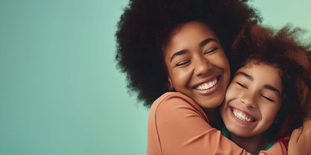 A mother and daughter share a warm embrace, both smiling brightly. Their natural curly hair frames their joyful faces as they express love and happiness. The background features a soft turquoise color, enhancing the cheerful atmosphere.の素材