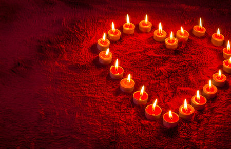 Heart-shaped candles arrangement on red background. Romantic and warm. Perfect for Valentine's Day.の写真素材