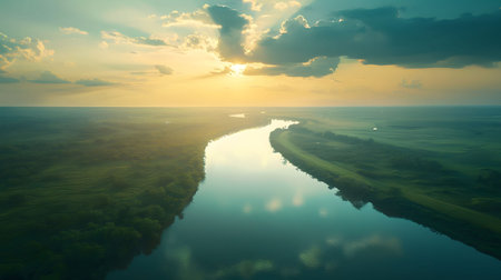 Stunning aerial shot of a river winding through a lush green landscape during a beautiful sunset. The tranquil scene is bathed in the warm glow of the setting sun.の写真素材